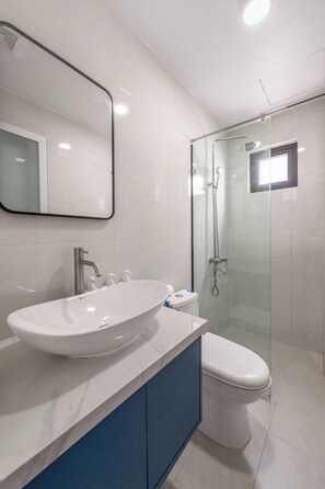 A modern bathroom with a large white sink, a toilet, and a glass-enclosed shower area. - V Hotel Da Nang  (Ngu Hanh Son)