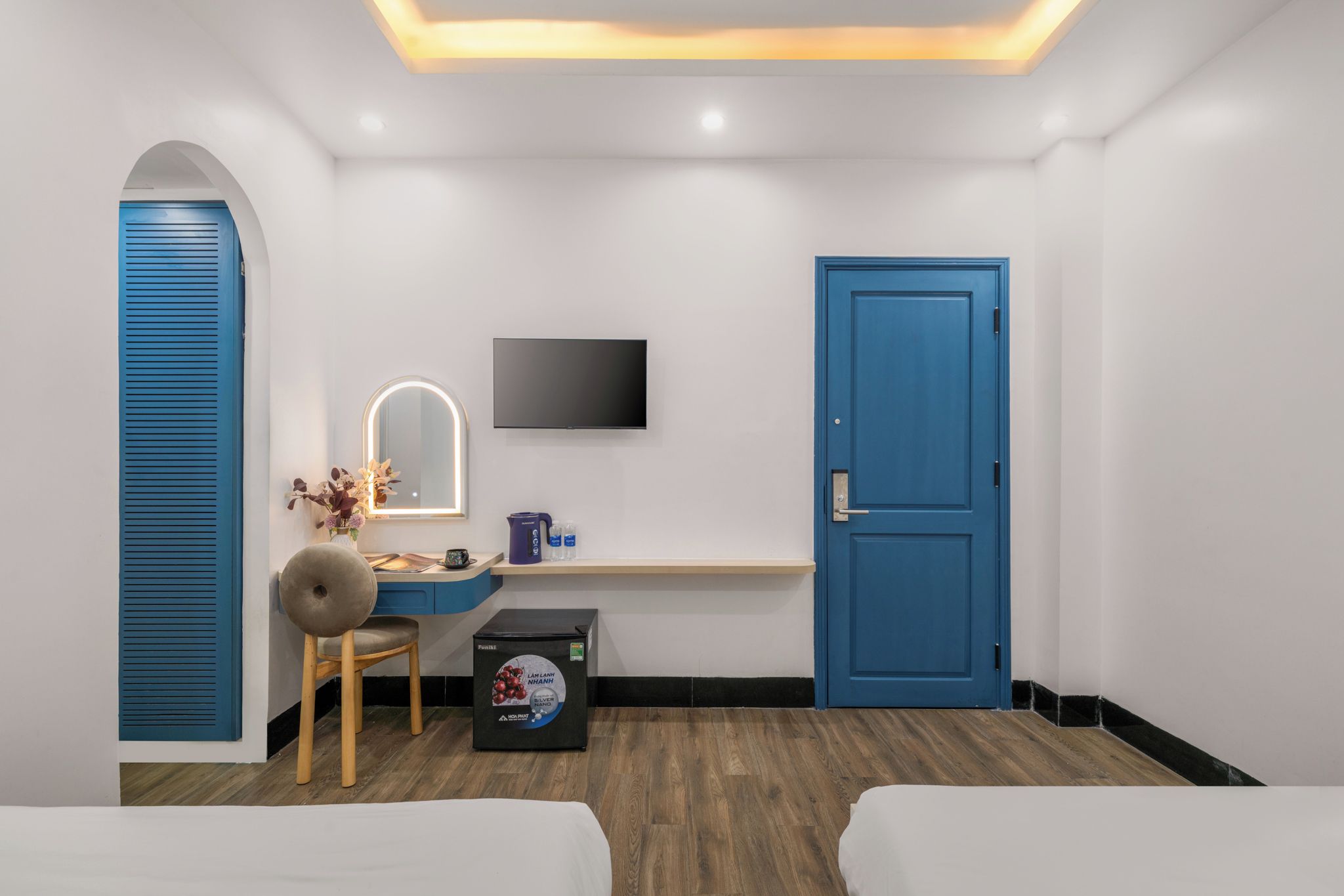 A modern bedroom with a desk, a TV, a blue door, and a bed.
