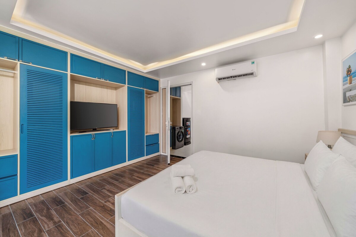 A hotel room with a bed, a television, a washing machine, and a ceiling light.