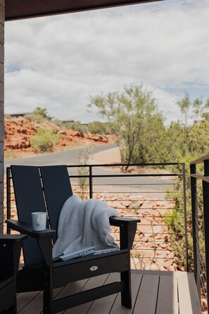 Ein Liegestuhl mit Tasse und Decke auf einer Holzterrasse, mit Blick auf eine felsige Landschaft mit spärlicher Vegetation.