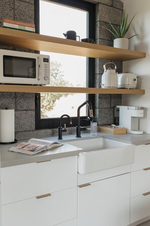 Eine moderne Küche mit Mikrowelle, Wasserkocher und Kaffeemaschine auf der Arbeitsfläche, einem Spülbecken mit Armatur und einem Fenster mit Blick auf Bäume.