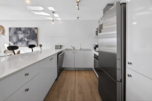 A modern kitchen with white cabinetry, a stainless steel refrigerator, and a wooden floor. - The Palmview Retreat - 800m to Hastings Street! (Noosa Heads)