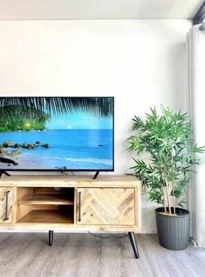 A flat-screen TV mounted on a wooden TV stand with a potted plant beside it. - The Palmview Retreat - 800m to Hastings Street! (Noosa Heads)