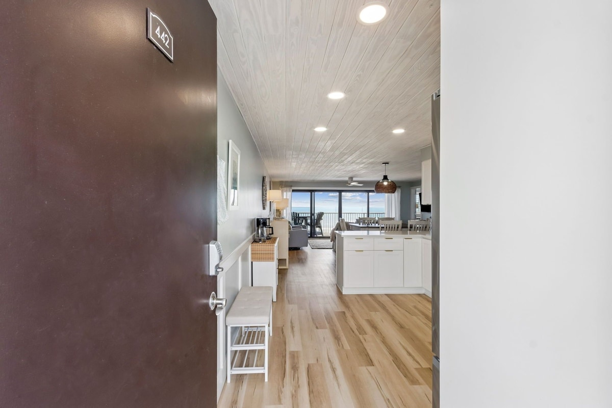 A modern kitchen with white cabinets, a wooden floor, and a view to the outside.