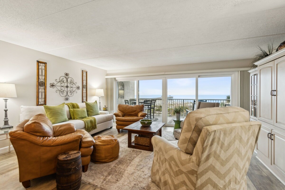 A living room with a sofa, armchairs, a coffee table, and a view of the ocean.