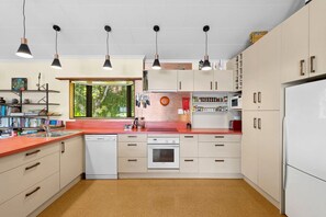 A kitchen with white cabinets, a red countertop, a dishwasher, an oven, and pendant lights. - Parapara Esplanade Stay (Takaka)