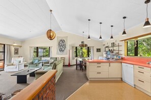 A spacious living area with a kitchen, dining area, and a view of greenery. - Parapara Esplanade Stay (Takaka)