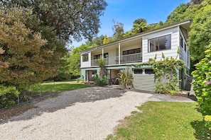 A two-story house with a front porch, a covered driveway, and a fenced yard. - Parapara Esplanade Stay (Takaka)