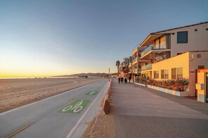 Eine Küstenstraße mit einem eigenen Radweg, neben einem mehrstöckigen Gebäude mit Balkonen und freiem Blick auf den Strand.