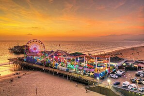 A pier with a Ferris wheel and amusement rides, adjacent to a beach with people and vehicles. - The Coastal Nest Beachside Getaway steps to Pier (Santa Monica)
