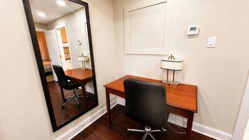 Quarto com escrivaninha de madeira, cadeira de escritório preta, espelho grande e luminária fixa na parede.