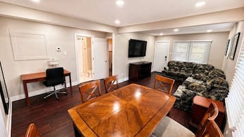 A conference room with a wooden table, chairs, a sofa, a TV, and a door leading to another room.