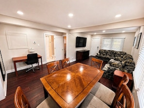 A conference room with a wooden table, chairs, a sofa, a TV, and a door leading to another room. - Niagara Riverside Villa Sleeps 8 Scenic Retreat (Niagara Falls)