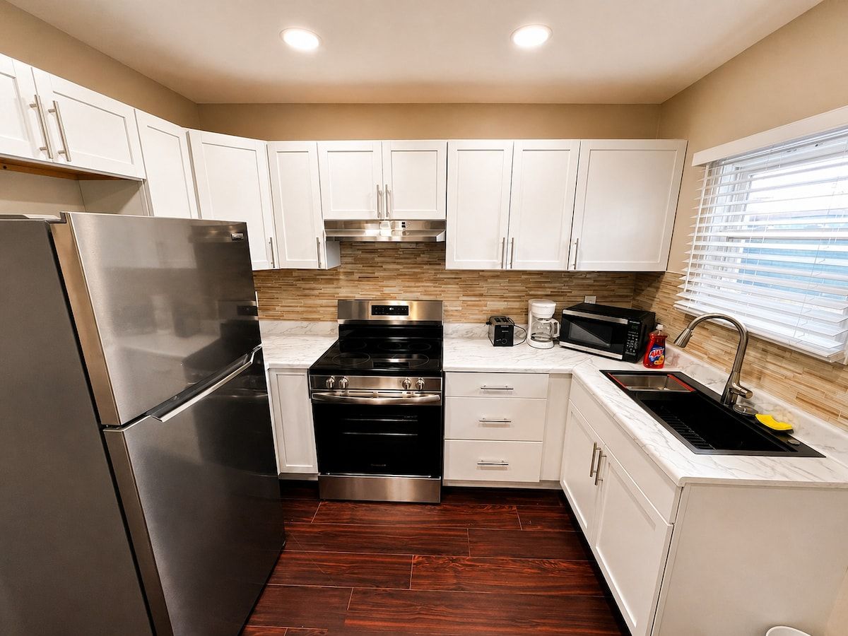 A compact kitchen with white cabinets, a stainless steel refrigerator, a stove, and a microwave.