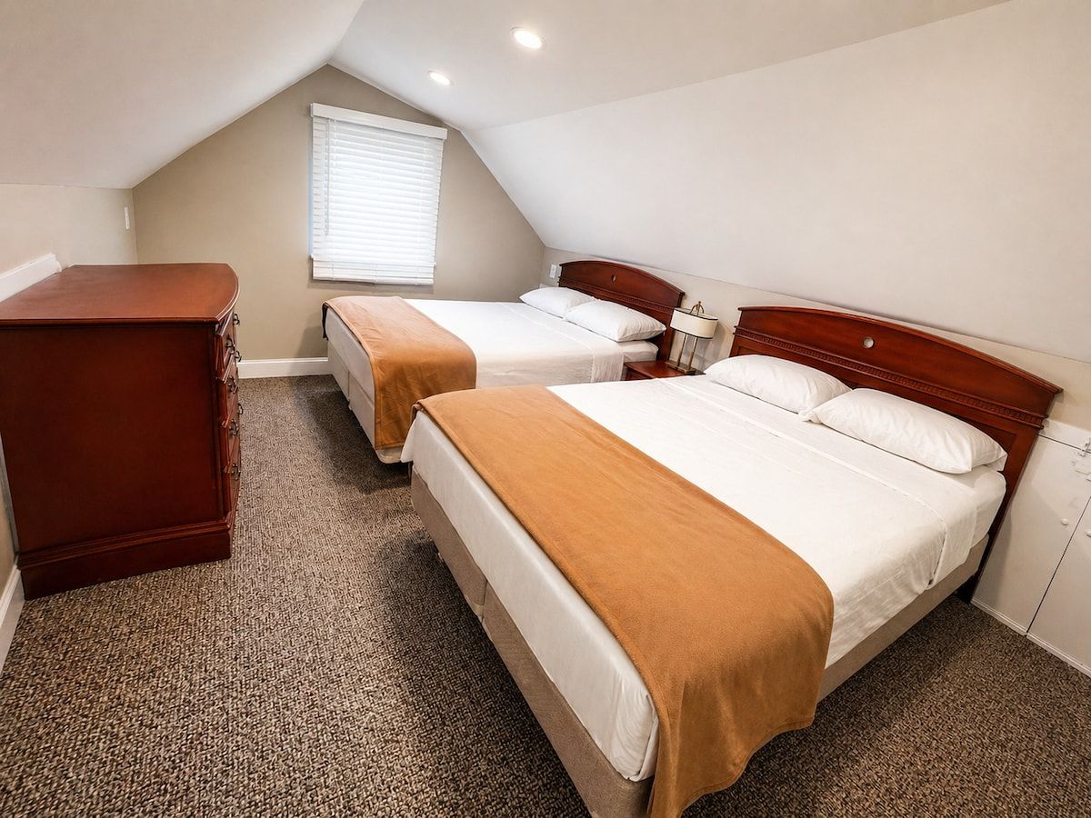 A hotel room with two beds, a dresser, and a window with blinds.