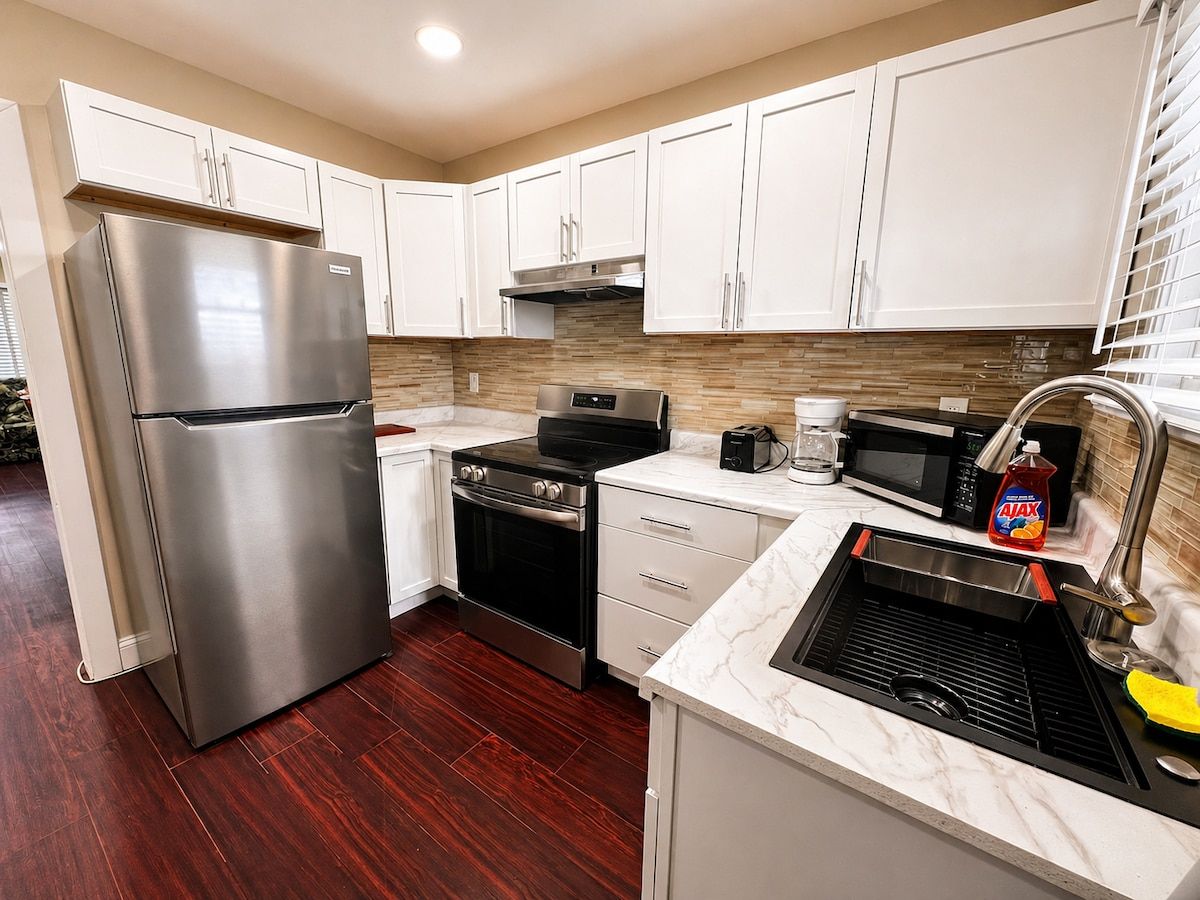 A modern kitchen with stainless steel appliances, white cabinetry, and a marble countertop.