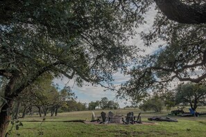 An outdoor seating area with chairs and a table, surrounded by trees and open space. - Guadalupe River Retreat (Seguin)
