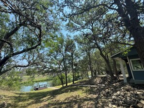 A lakeside cabin with a dock, surrounded by trees and a stone wall. - Guadalupe River Retreat (Seguin)