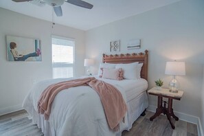 A bedroom with a bed, bedside lamps, a ceiling fan, a window with blinds, and wall art.