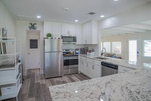 A modern kitchen with stainless steel appliances, white cabinetry, and a marble countertop. - Guadalupe River Retreat (Seguin)