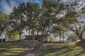 A house with a stone staircase leading to a porch, surrounded by trees. - Guadalupe River Retreat (Seguin)