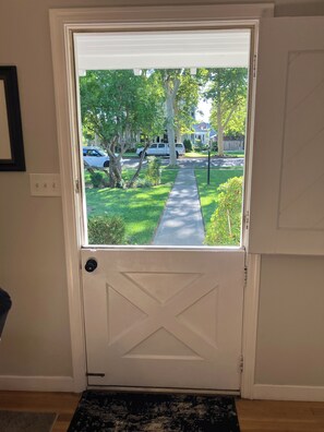 A white door with a view of a residential street, a sidewalk, and a grassy area.
