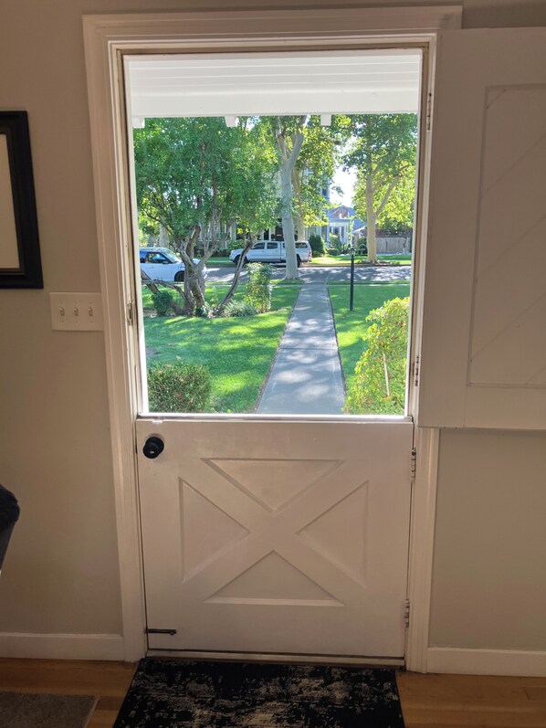 A white door with a view of a residential street, a sidewalk, and a grassy area.
