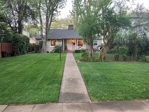 A residential property with a well-maintained lawn, a concrete pathway leading to the entrance, and a house with a visible number '1937' on the window.
