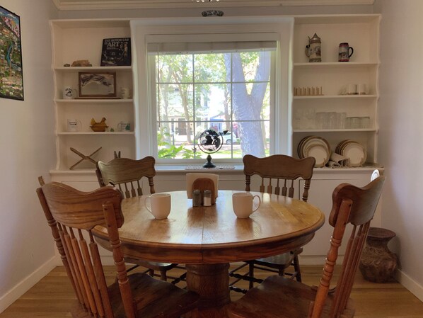 A dining area with a round wooden table, four chairs, and a window with a view of greenery outside.
