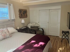 A hotel room with a bed, a chair, a desk, a lamp, a world map artwork, and a wardrobe.