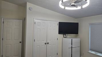 Ein Zimmer mit Deckenventilator, einem an der Wand montierten Flachbildfernseher und einem weißen Kleiderschrank.