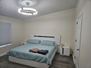 Un dormitorio con cama, mesitas de noche, un ventilador de techo y una puerta.
