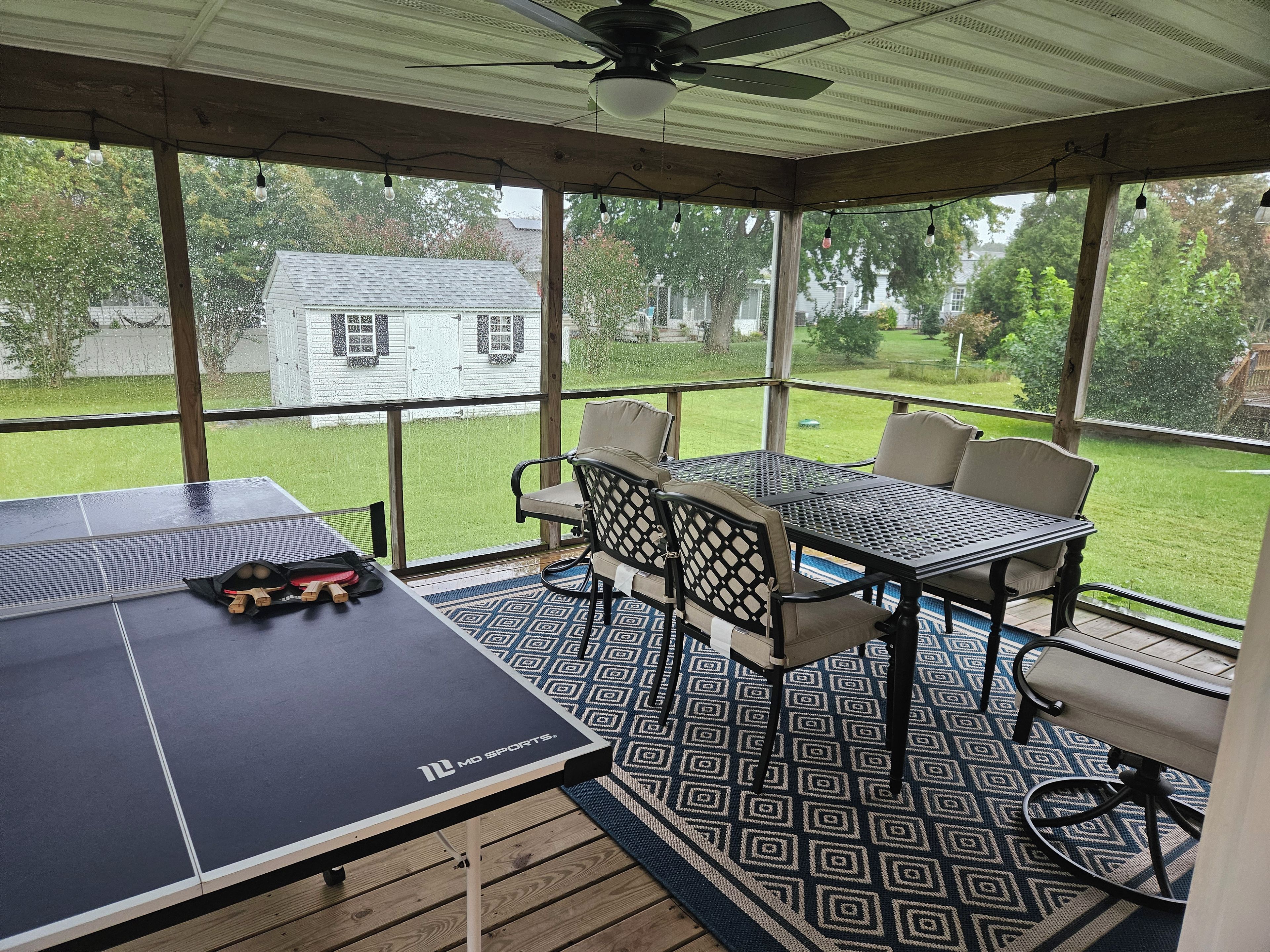 Ein überdachter Patio-Bereich mit Tischtennisplatte, Stühlen und Deckenventilator.