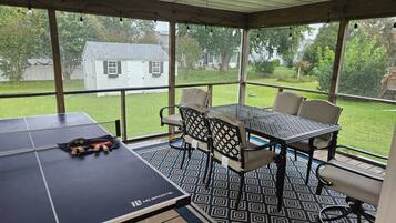 Ein überdachter Patio-Bereich mit Tischtennisplatte, Stühlen und Deckenventilator.