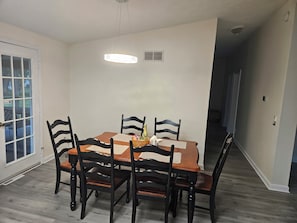 A dining area with a table set for four, surrounded by chairs, and a ceiling light fixture above.