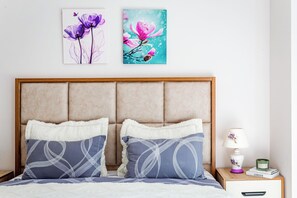 Una camera da letto con un letto, due cuscini, un comodino, una lampada e due opere d'arte a parete.