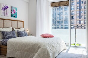 Ein Schlafzimmer mit einem großen Bett, Blick auf ein Gebäude durch ein Fenster und Kunstwerken an der Wand.