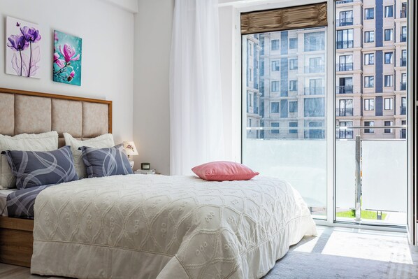 Ein Schlafzimmer mit einem großen Bett, Blick auf ein Gebäude durch ein Fenster und Kunstwerken an der Wand.
