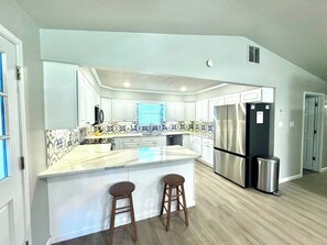 A modern kitchen with white cabinets, a stainless steel refrigerator, and a marble countertop. - Fish Haus-Seguin Texas (Seguin)