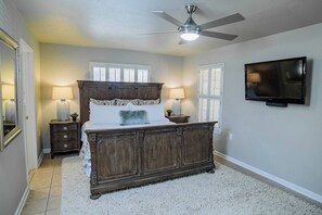 A bedroom with a large bed, two bedside tables with lamps, a ceiling fan, a television on the wall, and a window with shutters. - Fish Haus-Seguin Texas (Seguin)