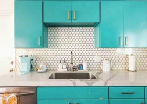 Une cuisine avec des armoires de couleur turquoise, un dosseret en carreaux hexagonaux et un évier en acier inoxydable.
