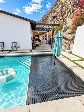 Una piscina con suelo de baldosas hexagonales, rodeada por un patio amueblado y una pérgola.