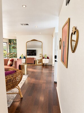 Un salon moderne avec un canapé, une table basse et un téléviseur. Des objets décoratifs sont disposés sur les étagères et un miroir est accroché au mur.