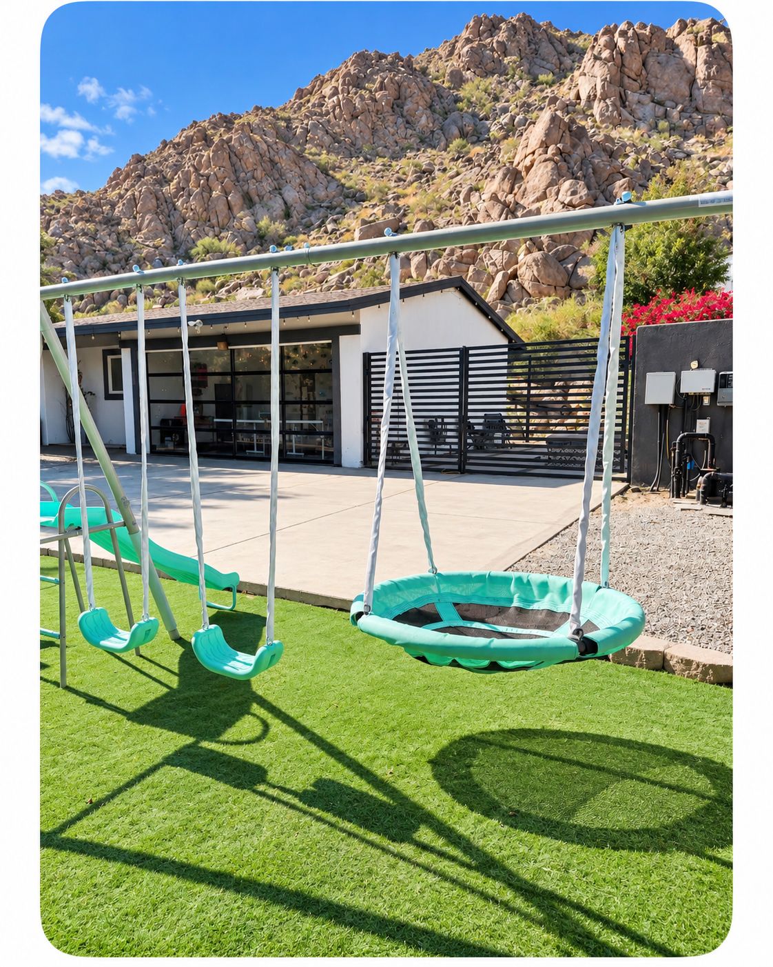 A playground with swings and a small pool, set against a backdrop of a building and rocky terrain.