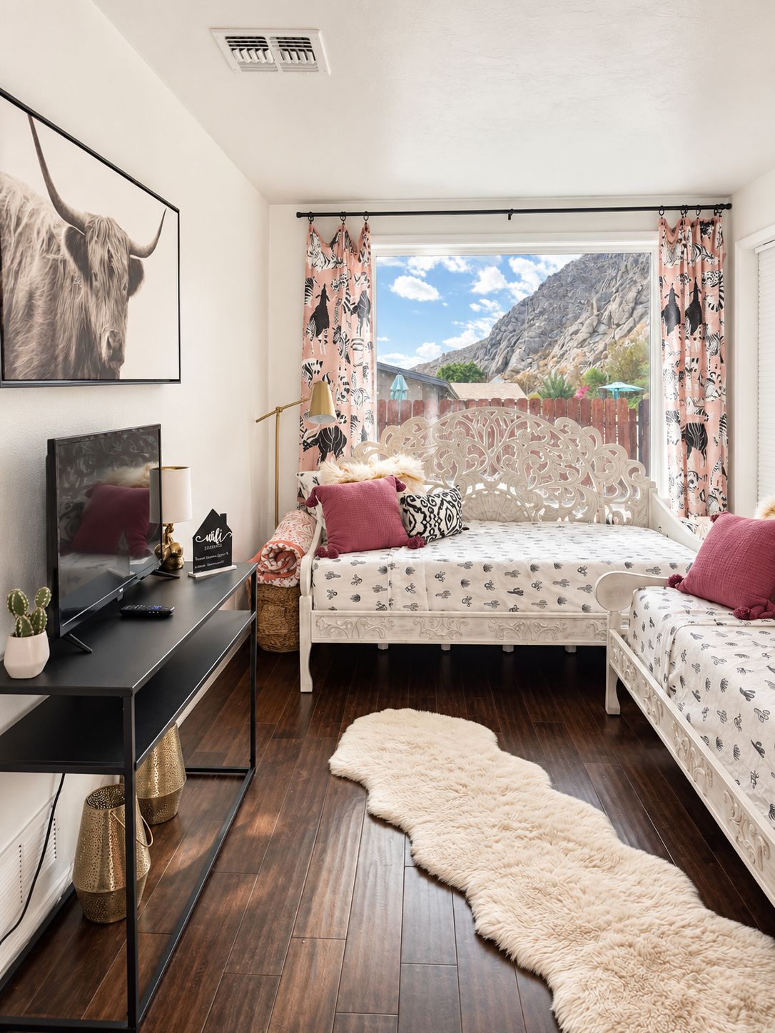 A bedroom with a bed, a TV, a desk, and a view of a mountainous landscape.