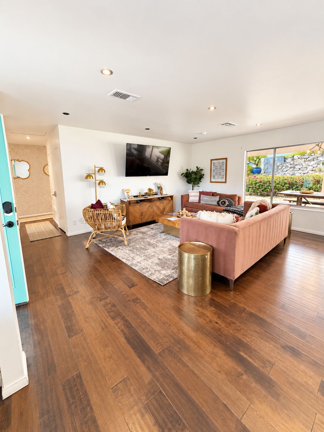 A spacious living room with a flat-screen TV, a pink sofa, and a wooden floor.