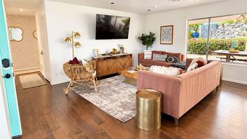 A spacious living room with a flat-screen TV, a pink sofa, and a wooden floor.