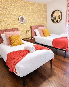 Habitación de hotel con dos camas, un espejo redondo, un reloj de pared y un pequeño estante con objetos decorativos.