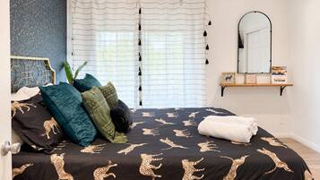 A bedroom with a bed featuring a leopard print bedspread, a headboard with a geometric pattern, a potted plant, and a mirror on the wall.