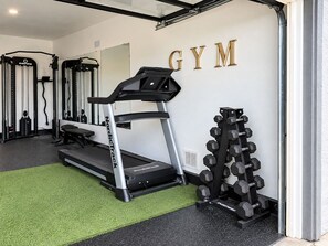 Un gimnasio con cinta de correr, banco de pesas y mancuernas.